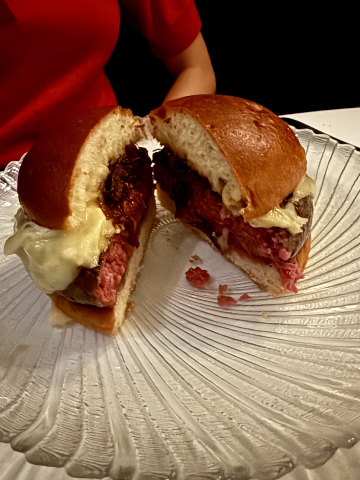 Cross-section of Le Burger at Le B., showing a rare-cooked dry-aged Angus patty, a brie-style cheese cascade, and a compact brioche bun