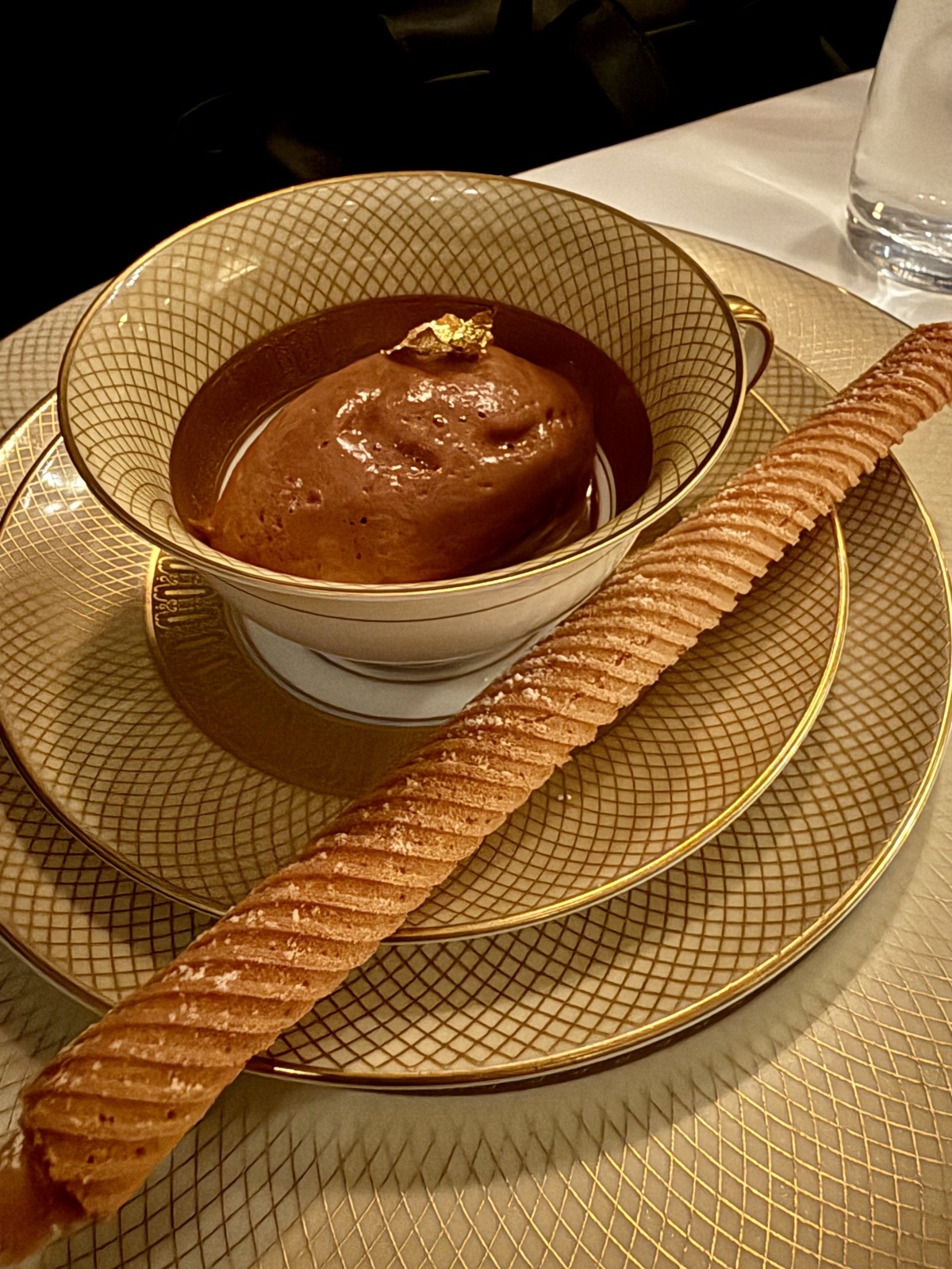 Chocolate mousse at Le B., topped with gold leaf, served in a gold-rimmed lattice-patterned porcelain cup with a long ridged pastry cigar on the side