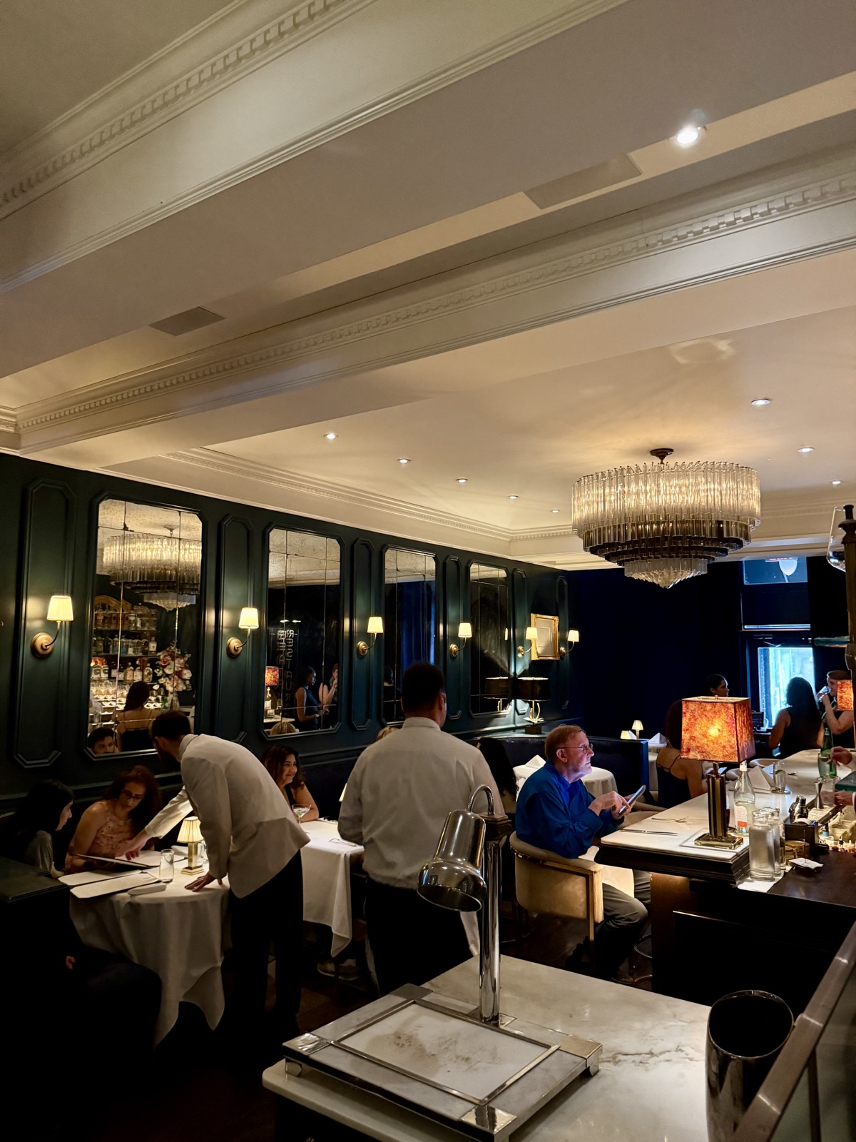 Le B. dining room with deep teal walls, antiqued mirrors, and a tiered glass chandelier