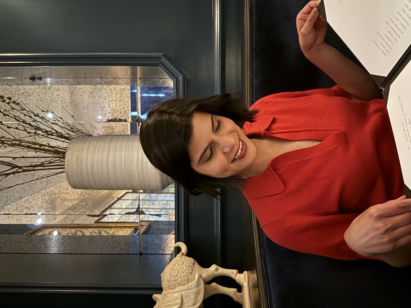 A guest in a red sweater smiles at the Le B. menu in a candlelit dining room